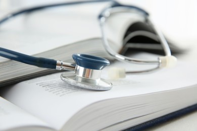 One new medical stethoscope and books on white wooden table, closeup