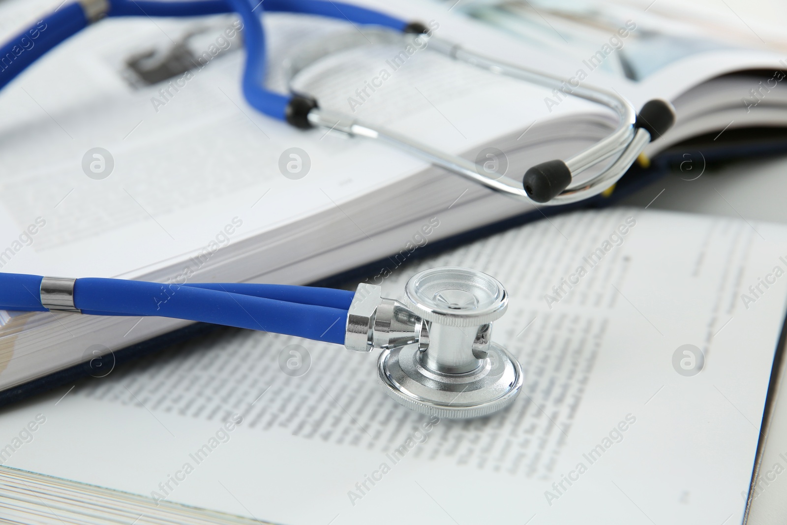 Photo of One medical stethoscope and books on table, closeup