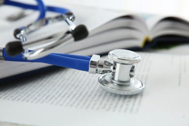 Photo of One medical stethoscope and books on table, closeup