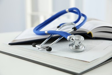 One medical stethoscope and books on white table, closeup