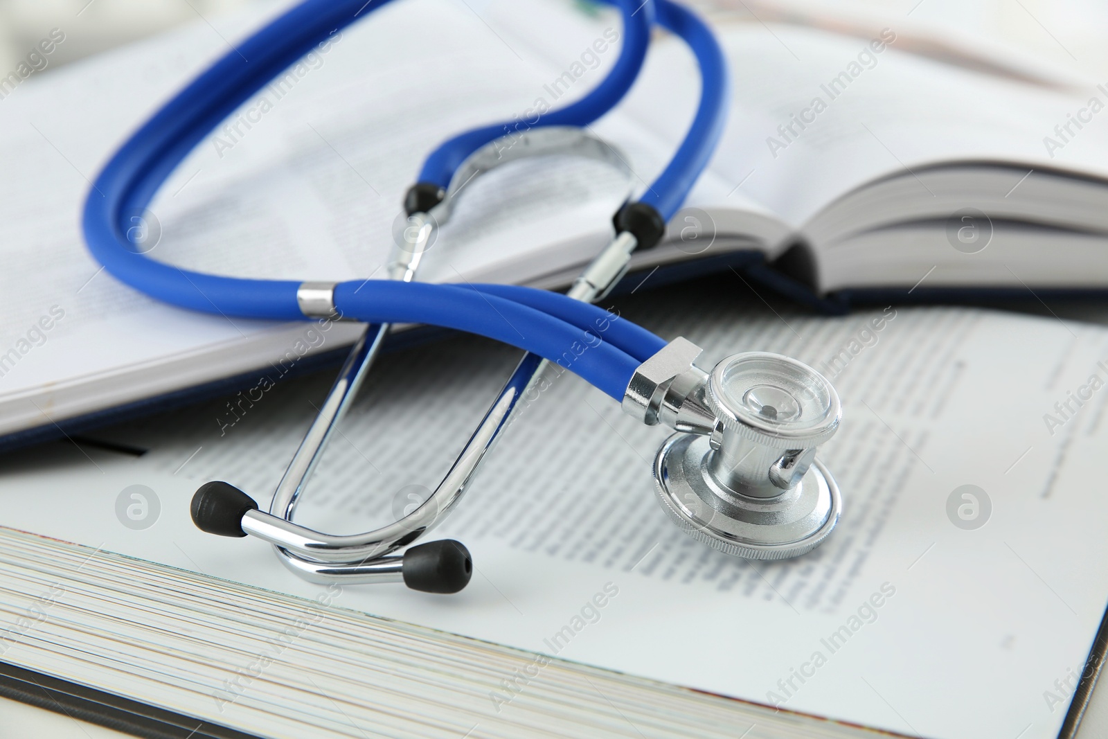 Photo of One medical stethoscope and books on white table, closeup