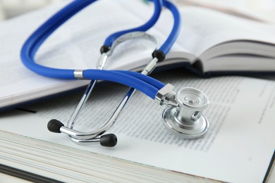 Photo of One medical stethoscope and books on white table, closeup