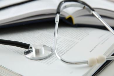 Photo of One medical stethoscope and books on white table, closeup