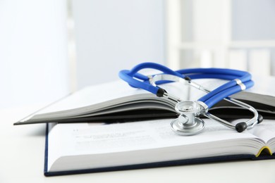 One medical stethoscope and books on white table, closeup