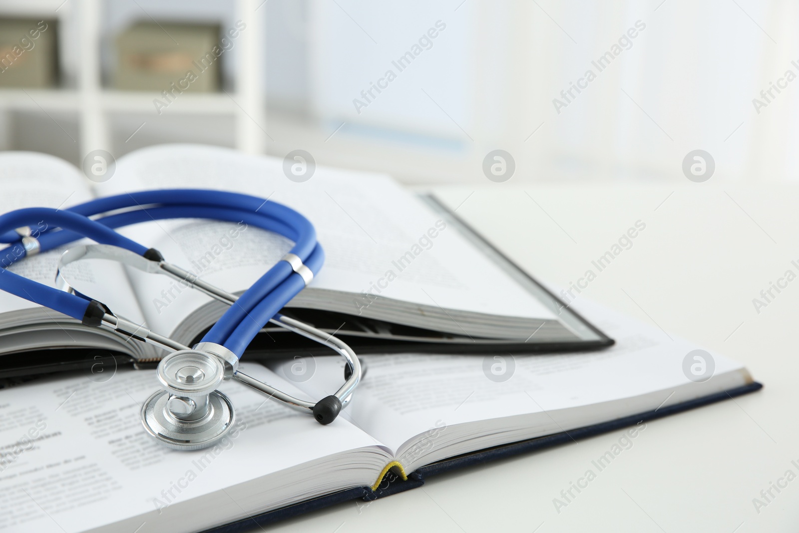 Photo of One medical stethoscope and books on white table, closeup