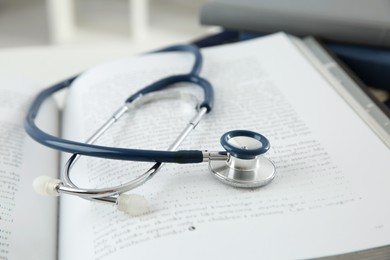 Photo of One medical stethoscope and books on white table, closeup