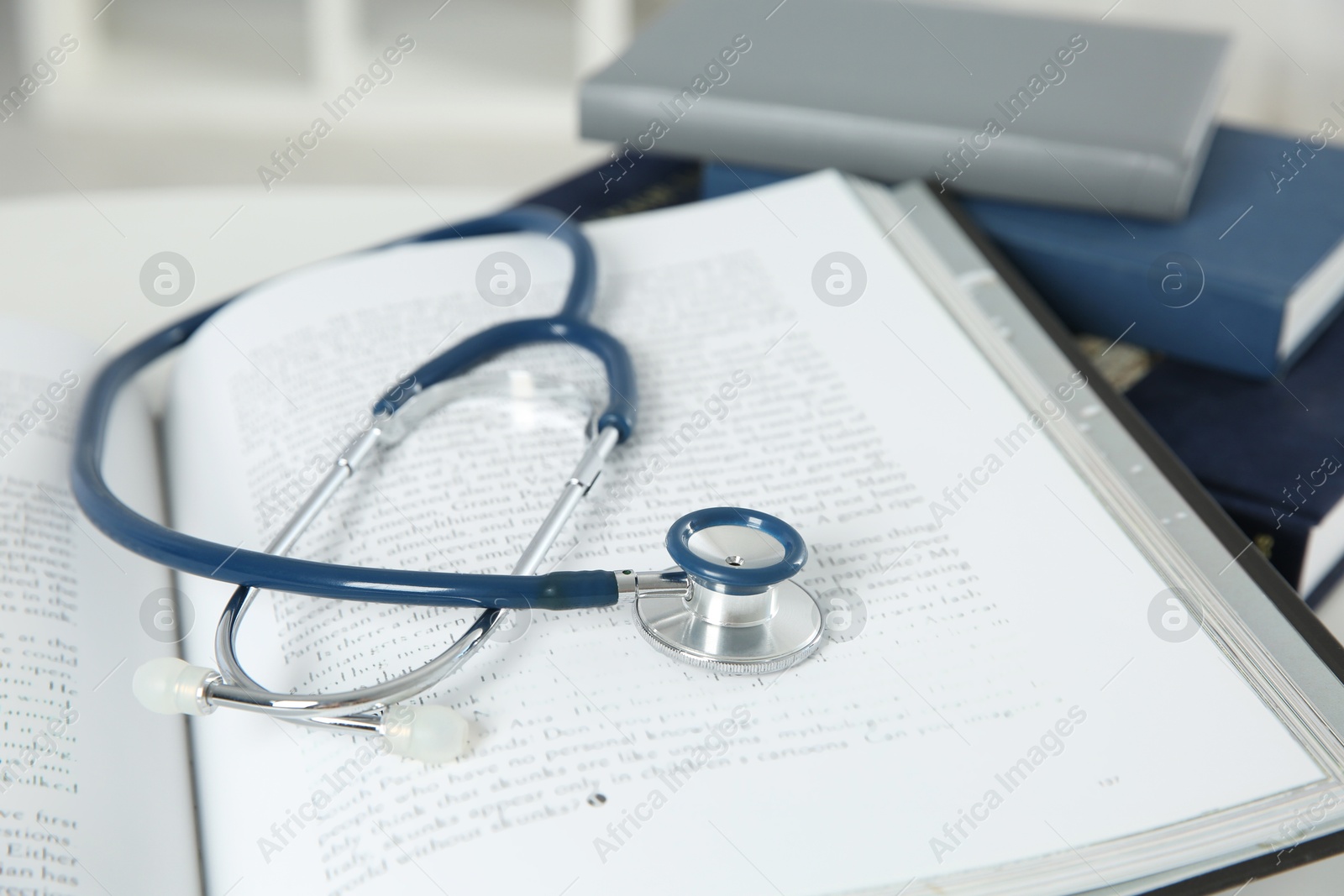 Photo of One medical stethoscope and books on white table, closeup