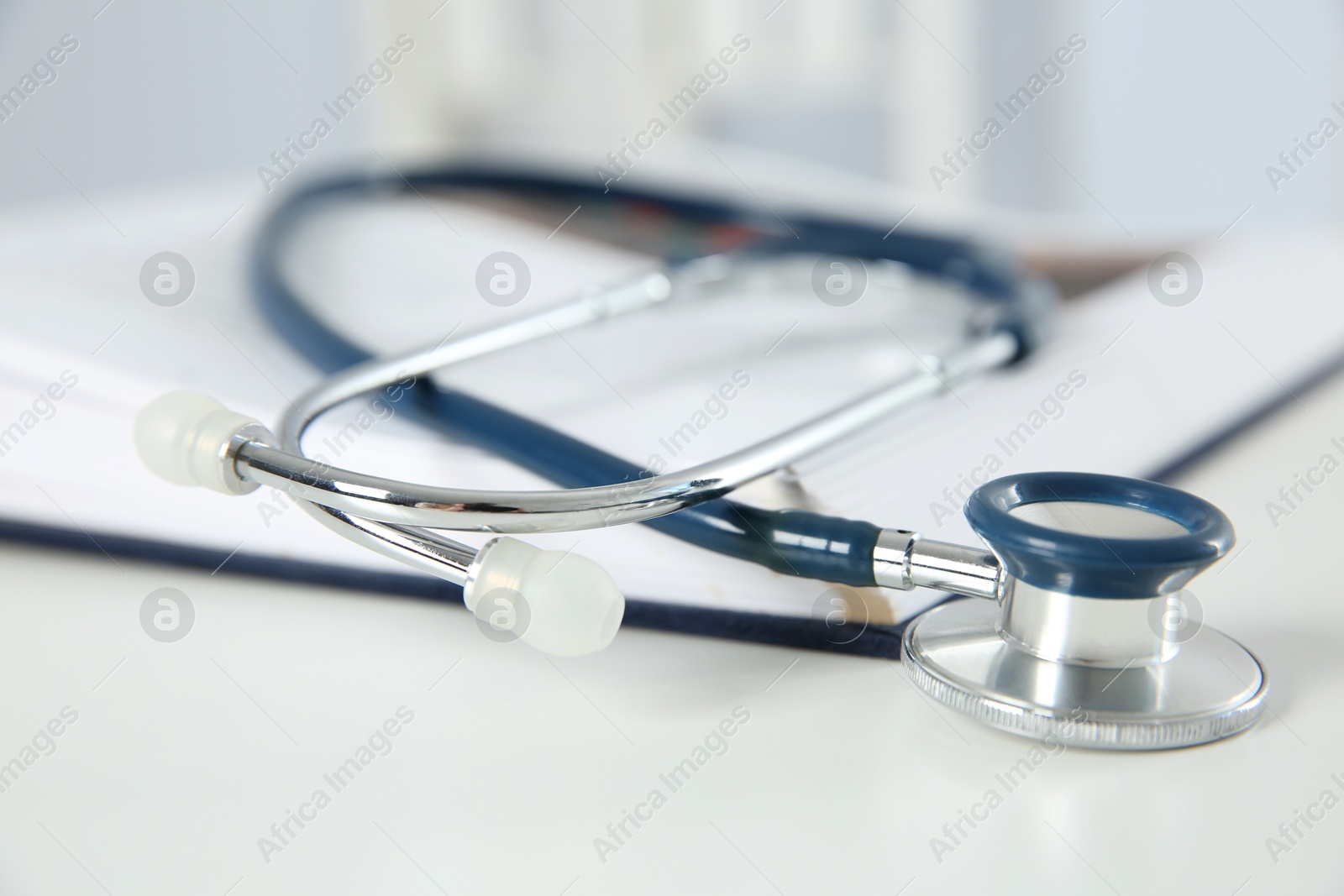 Photo of One medical stethoscope and book on white table, closeup