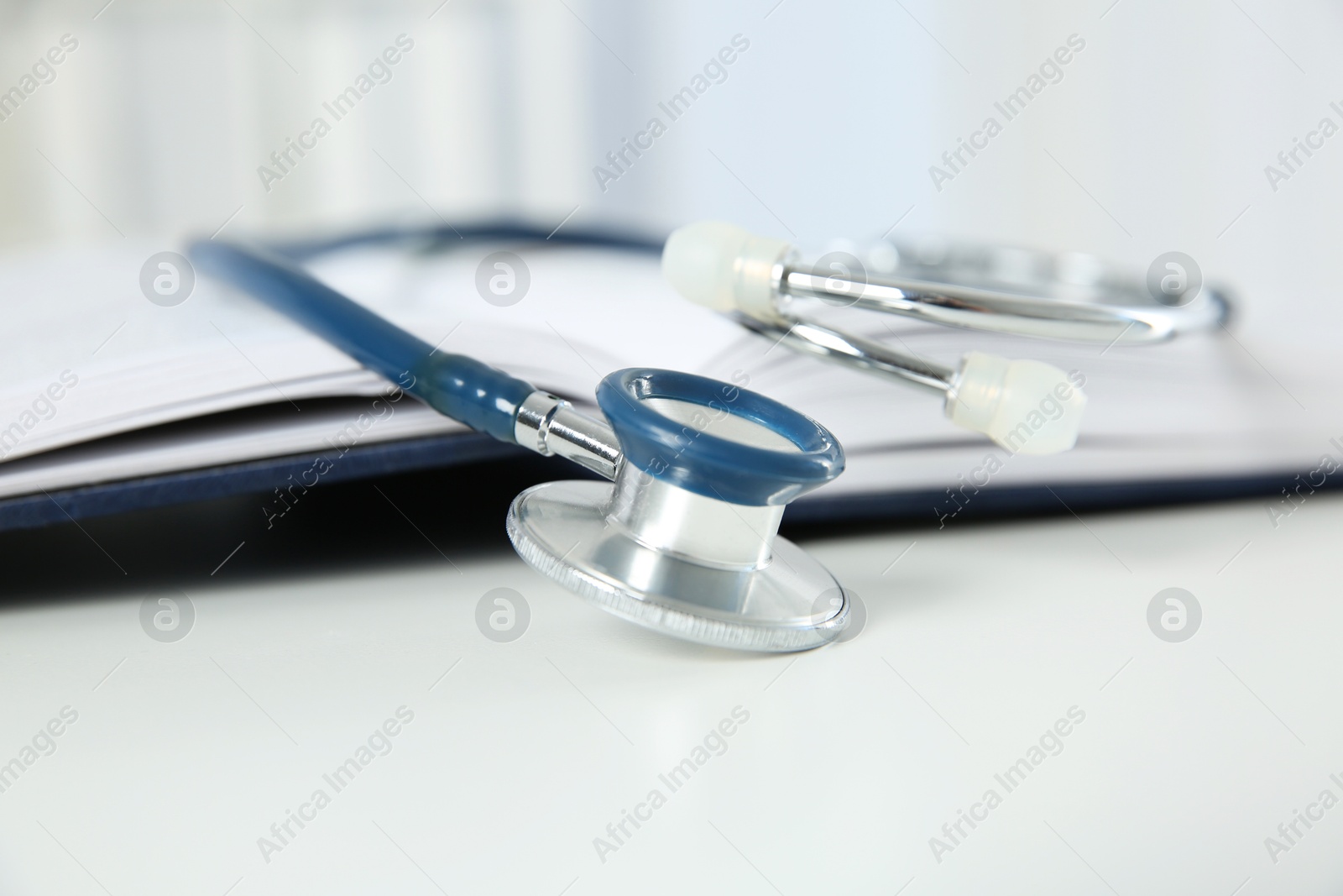 Photo of One medical stethoscope and book on white table, closeup