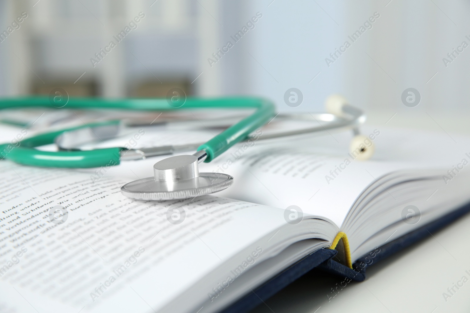 Photo of One medical stethoscope and book on white table, closeup