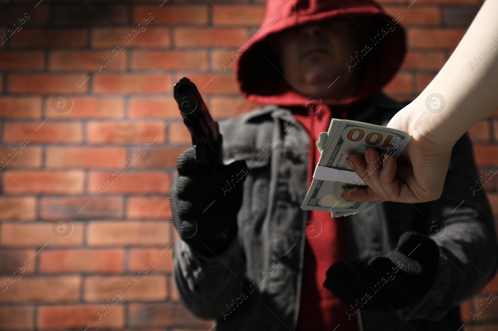 Photo of Woman giving money to criminal with gun near brick wall, closeup. Armed robbery