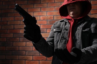 Photo of Dangerous criminal with gun near brick wall. Armed robbery