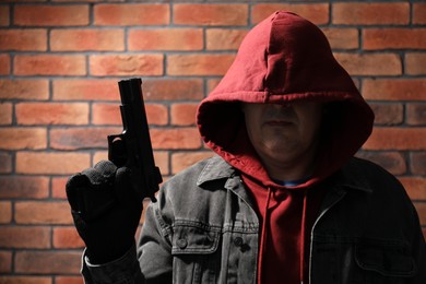 Photo of Dangerous criminal with gun near brick wall. Armed robbery