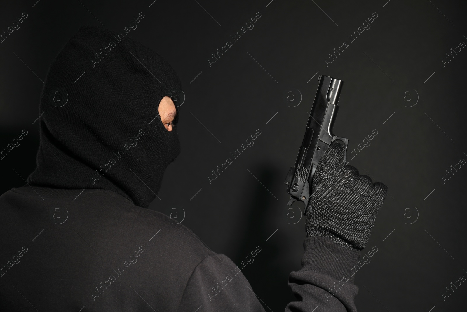 Photo of Dangerous masked criminal with gun on black background. Armed robbery