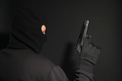 Photo of Dangerous masked criminal with gun on black background. Armed robbery