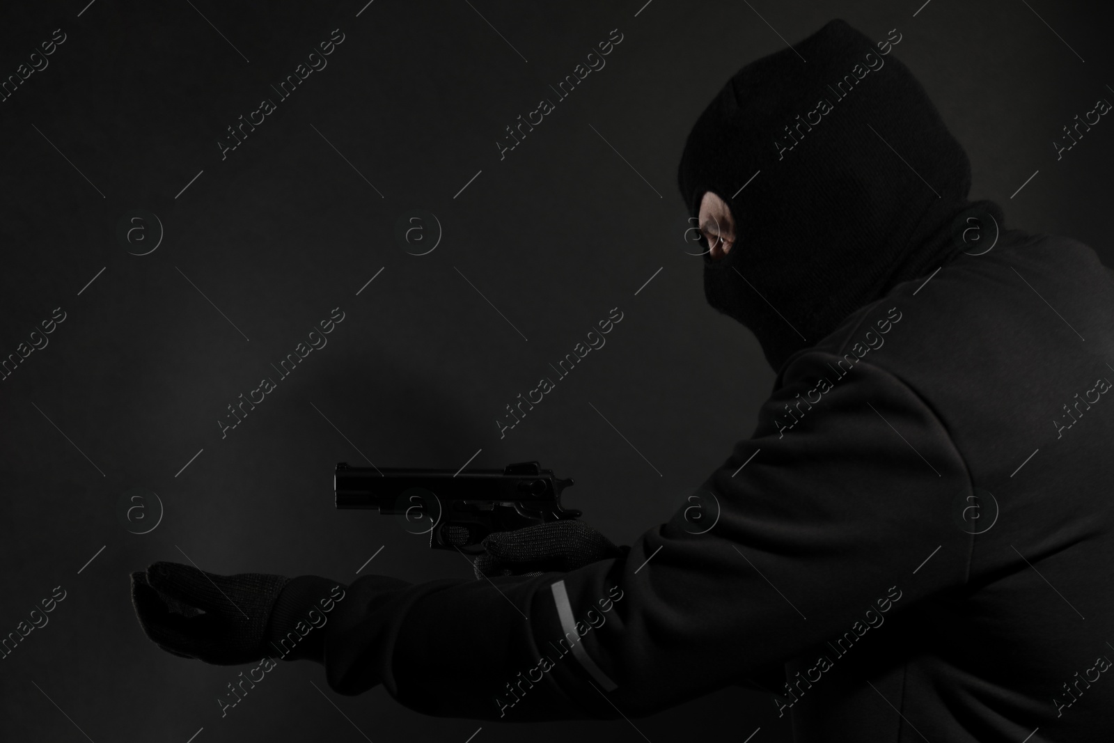 Photo of Dangerous masked criminal with gun on black background. Armed robbery