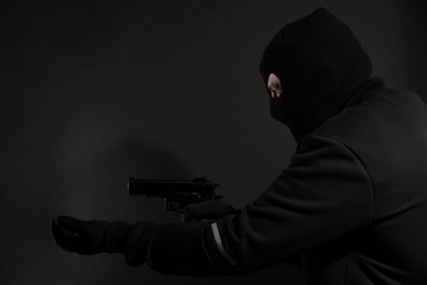 Dangerous masked criminal with gun on black background. Armed robbery