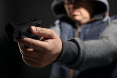 Dangerous criminal with gun on black background, selective focus. Armed robbery