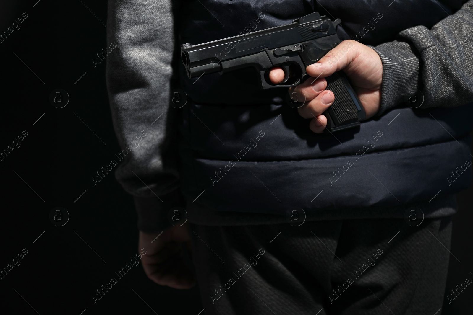 Photo of Man hiding gun behind his back on black background, closeup. Armed robbery