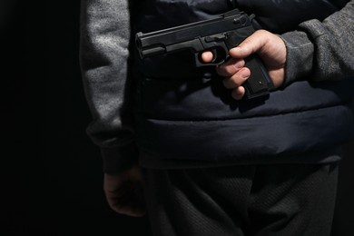 Photo of Man hiding gun behind his back on black background, closeup. Armed robbery