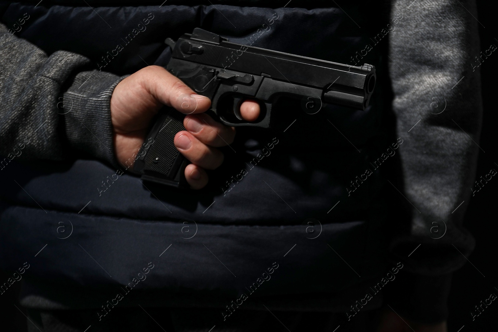 Photo of Man hiding gun behind his back on black background, closeup. Armed robbery