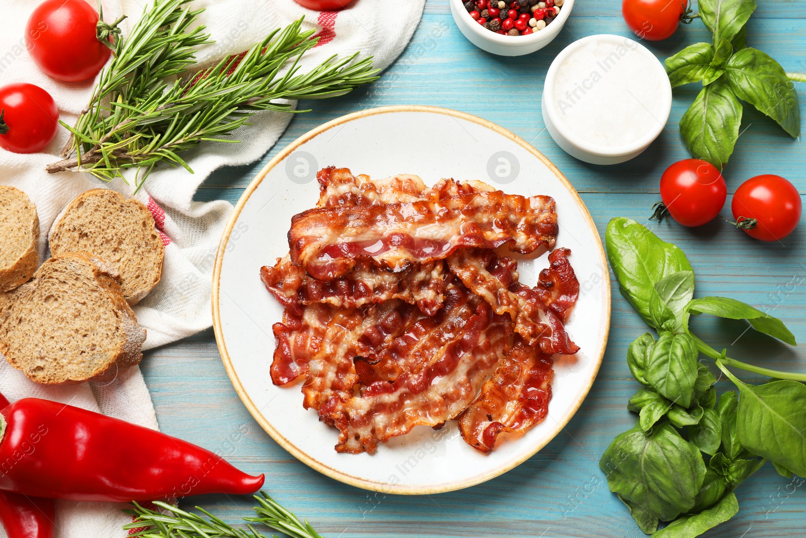 Photo of Slices of tasty fried bacon, tomatoes, different spices and bread on light blue wooden table, top view