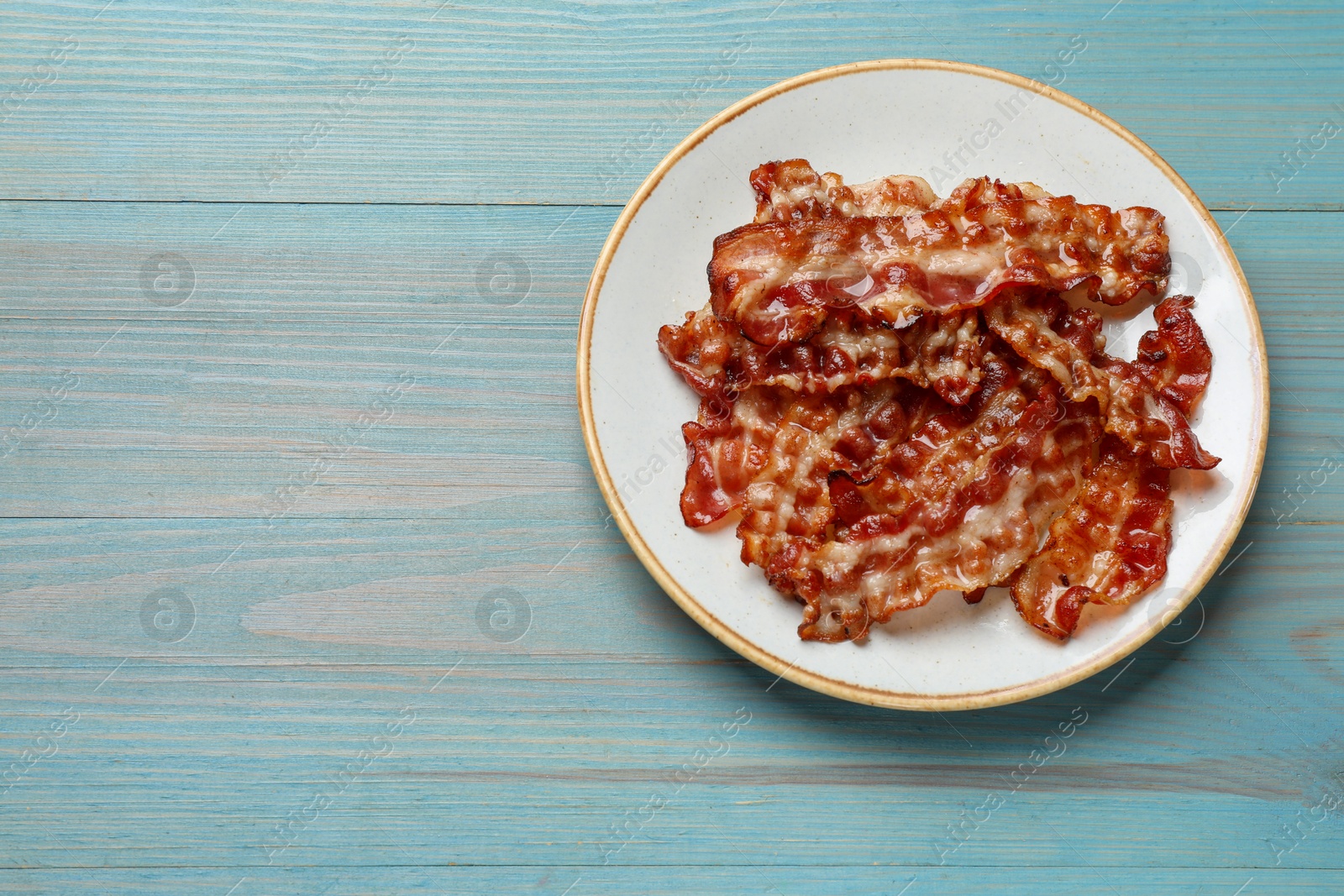 Photo of Slices of tasty fried bacon on light blue wooden table, top view. Space for text