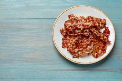 Photo of Slices of tasty fried bacon on light blue wooden table, top view. Space for text