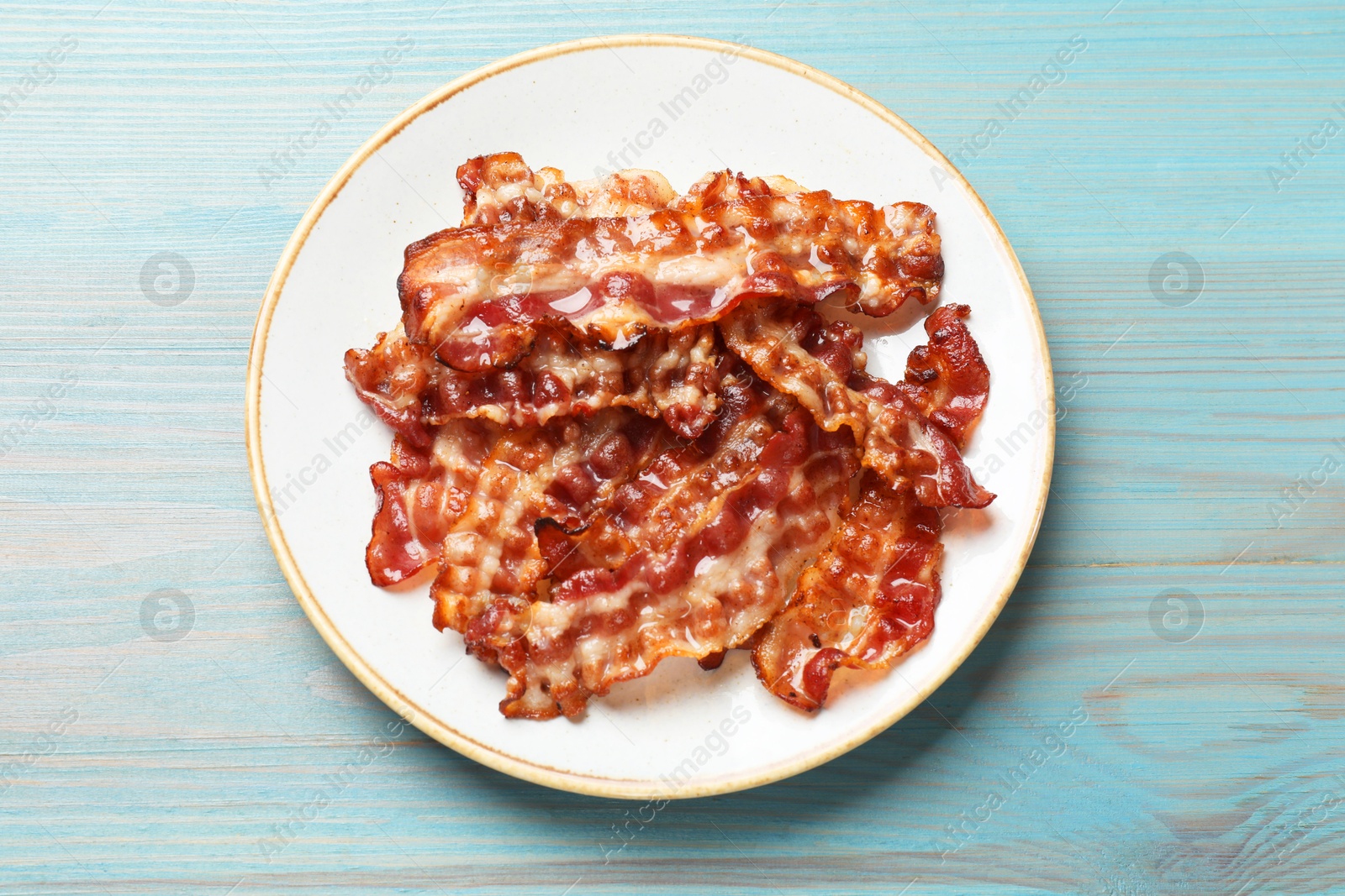 Photo of Slices of tasty fried bacon on light blue wooden table, top view