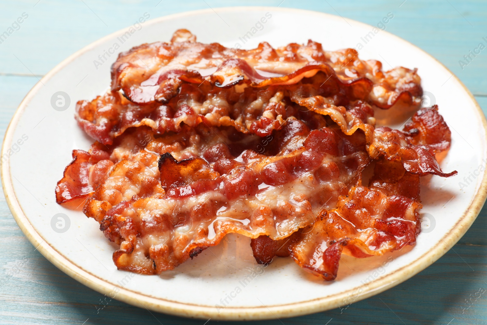 Photo of Slices of tasty fried bacon on light blue wooden table, closeup