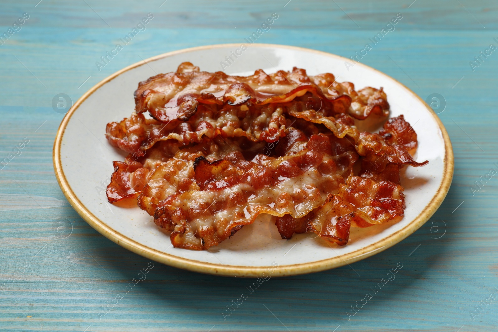 Photo of Slices of tasty fried bacon on light blue wooden table