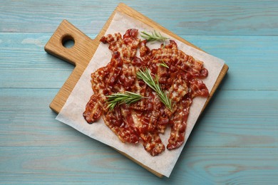 Photo of Slices of tasty fried bacon and rosemary on light blue wooden table, top view