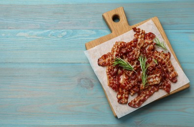 Photo of Slices of tasty fried bacon and rosemary on light blue wooden table, top view. Space for text