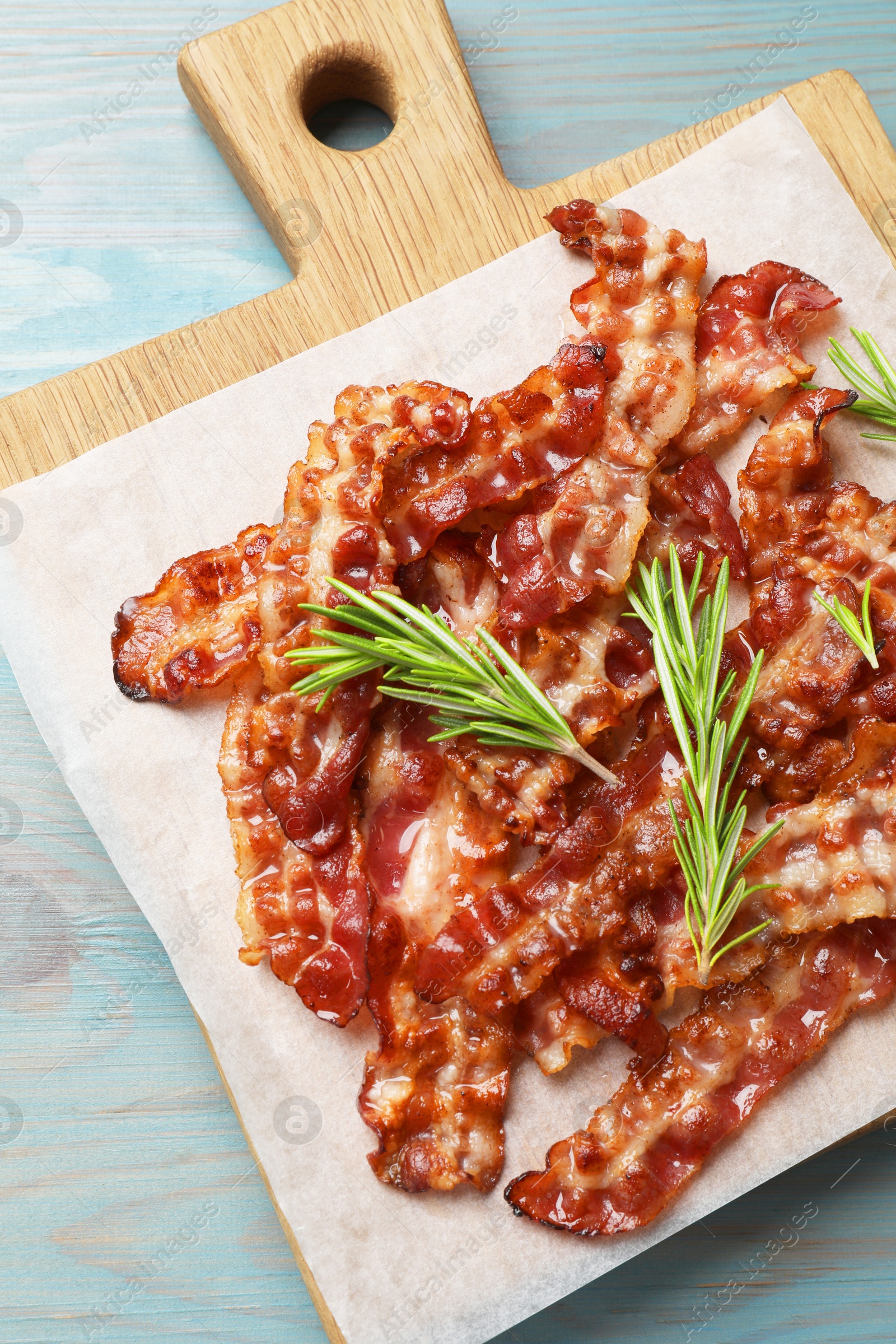 Photo of Slices of tasty fried bacon and rosemary on light blue wooden table, top view