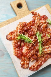 Photo of Slices of tasty fried bacon and rosemary on light blue wooden table, top view