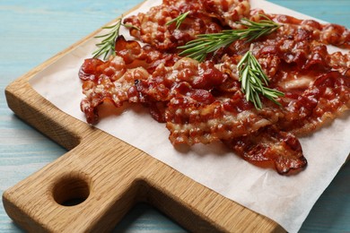 Photo of Slices of tasty fried bacon and rosemary on light blue wooden table, closeup