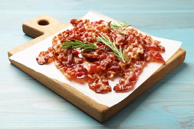 Photo of Slices of tasty fried bacon and rosemary on light blue wooden table