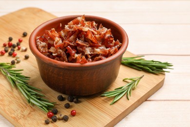 Photo of Pieces of tasty fried bacon in bowl and spices on wooden table, closeup