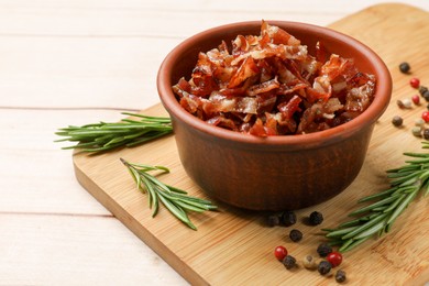 Photo of Pieces of tasty fried bacon in bowl and spices on wooden table, closeup