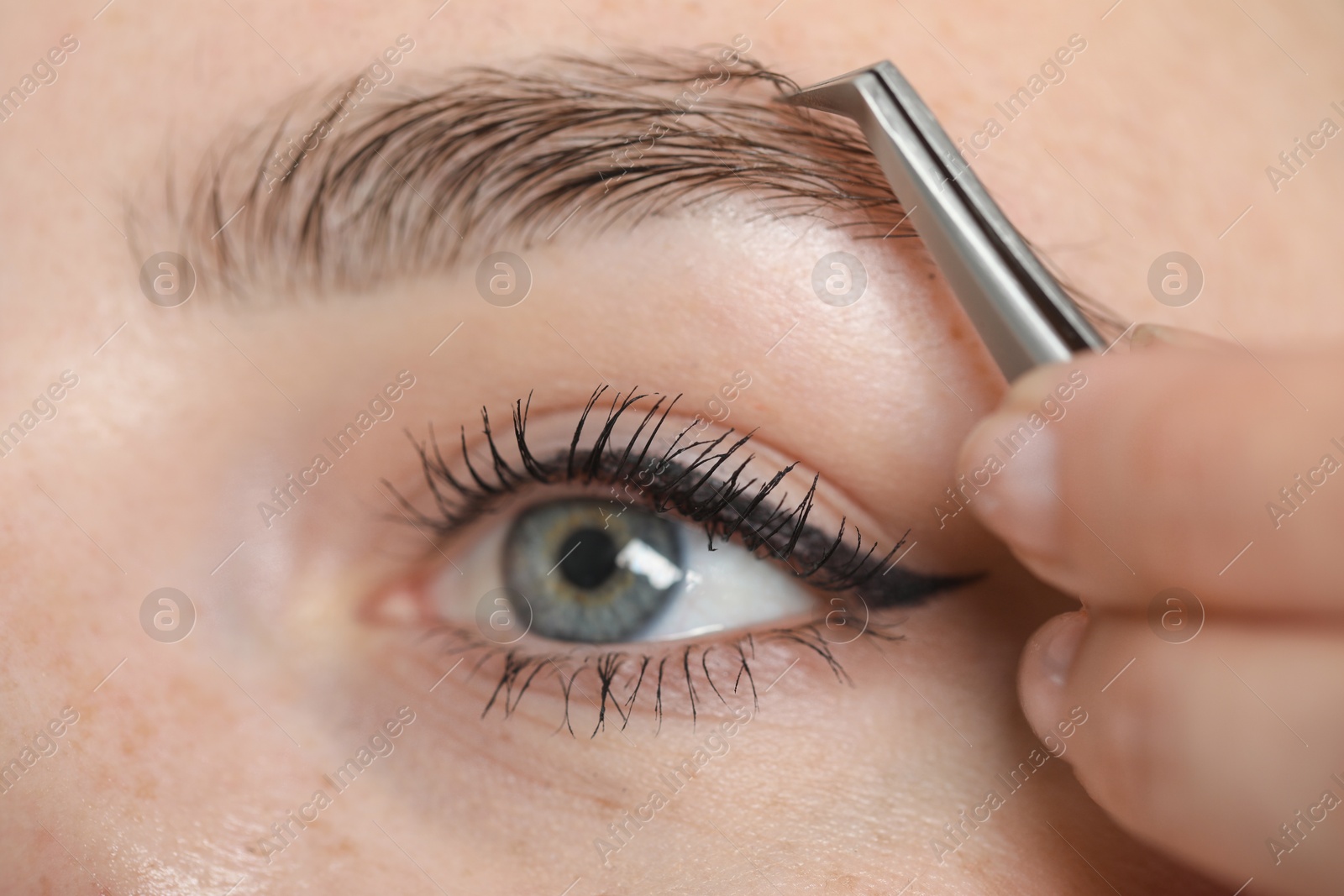 Photo of Beautician plucking young woman's eyebrow, closeup view