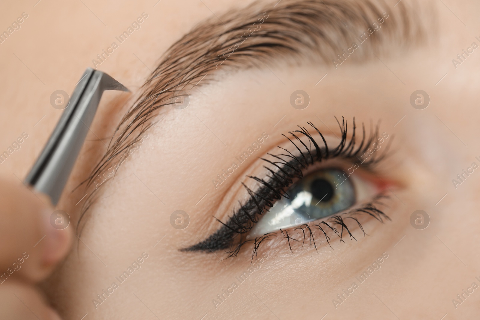 Photo of Beautician plucking young woman's eyebrow, closeup view