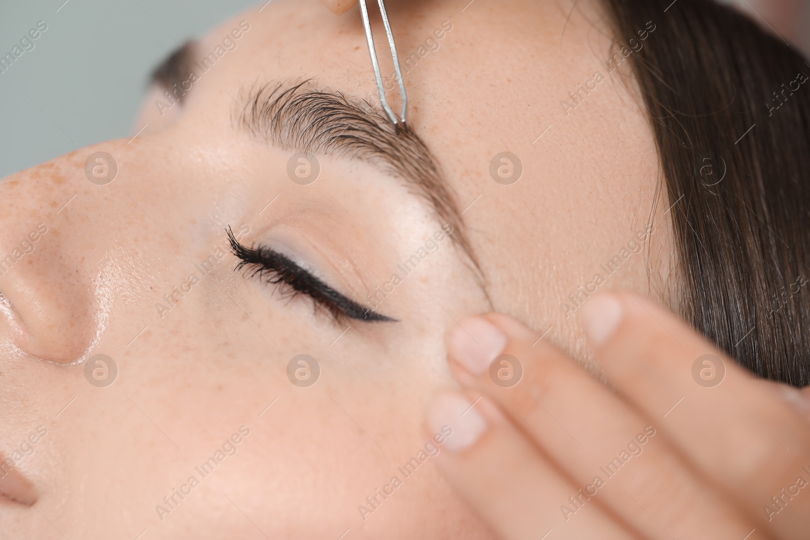 Photo of Beautician plucking young woman's eyebrow, closeup view