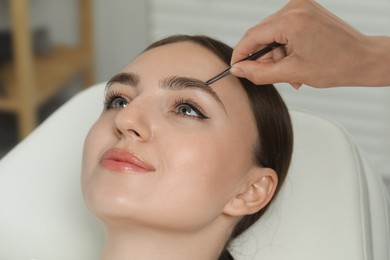Photo of Beautician plucking young woman's eyebrow in beauty salon, closeup