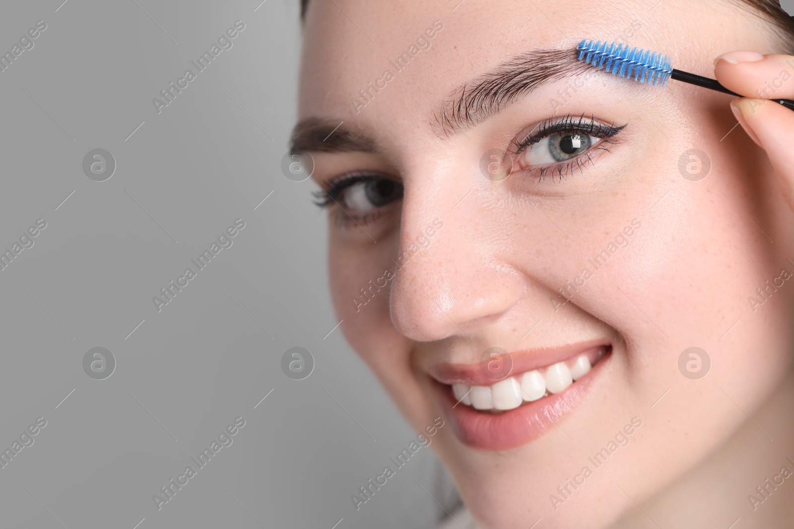 Photo of Young woman with spoolie brush on light background, closeup. Eyebrow correction