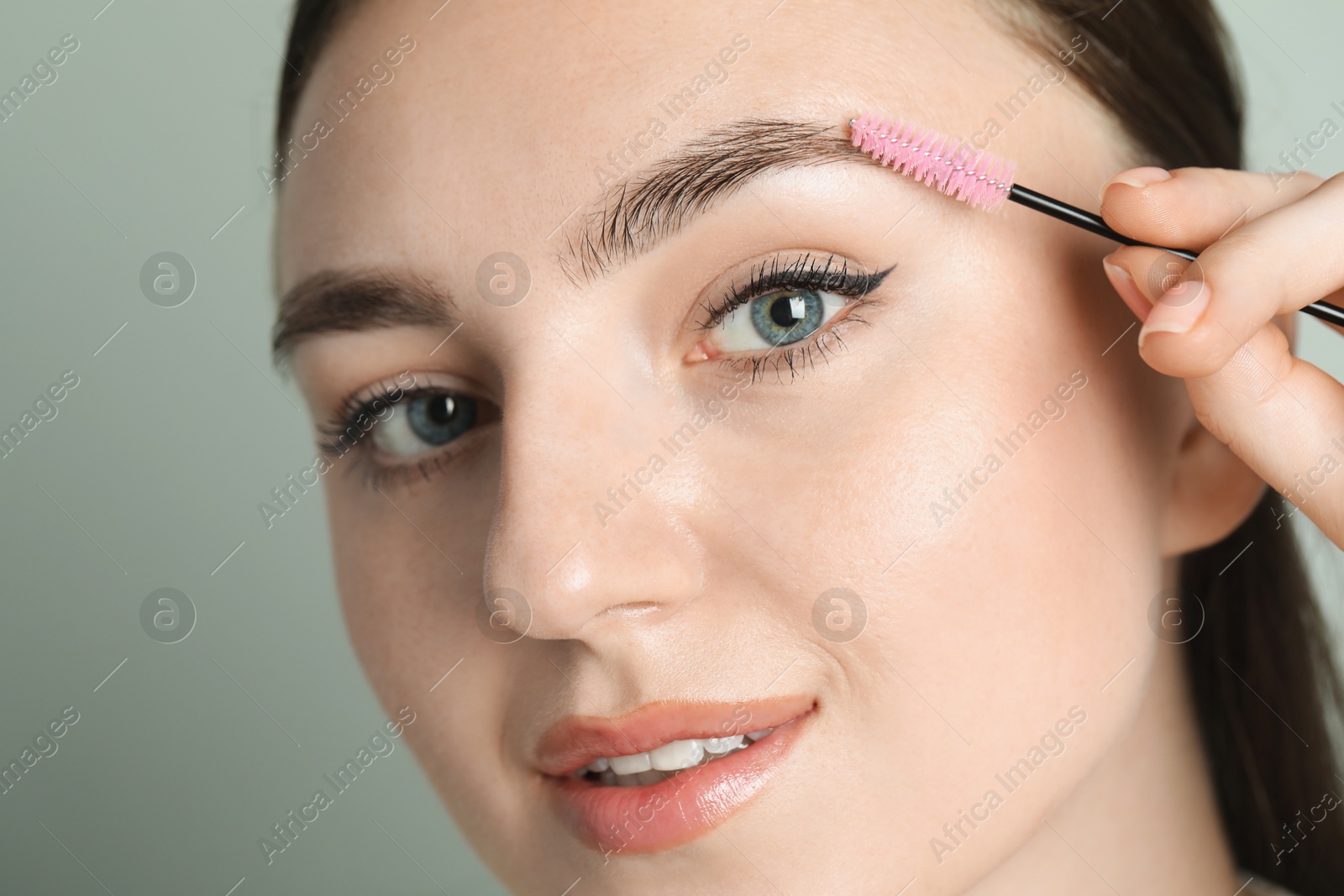 Photo of Young woman with spoolie brush on light background, closeup. Eyebrow correction