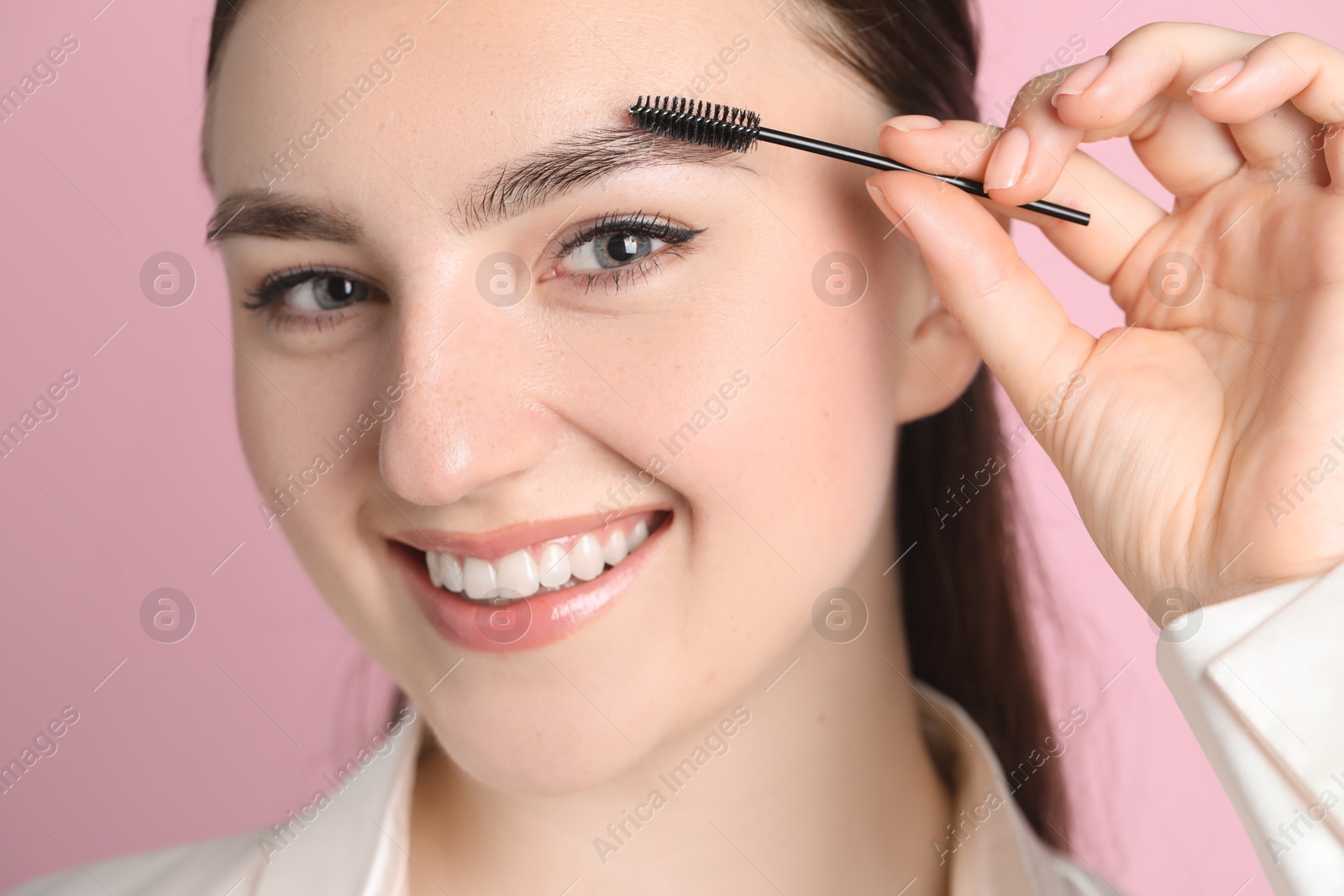 Photo of Young woman brushing eyebrow on pink background, closeup