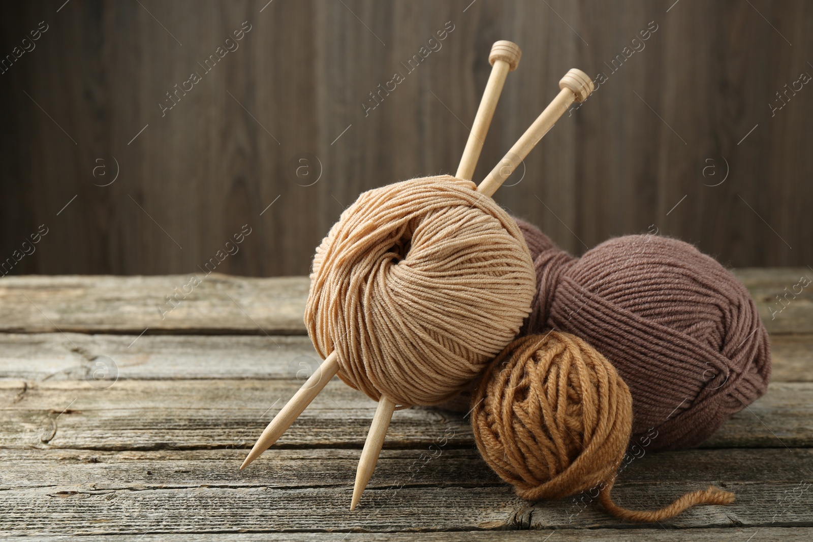 Photo of Skeins of soft yarn and knitting needles on wooden table, space for text