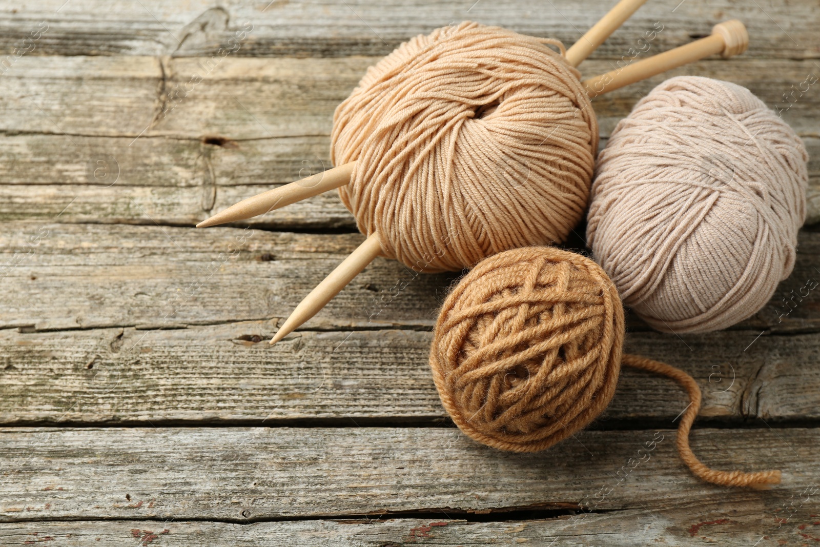 Photo of Skeins of soft yarn and knitting needles on wooden table, above view. Space for text