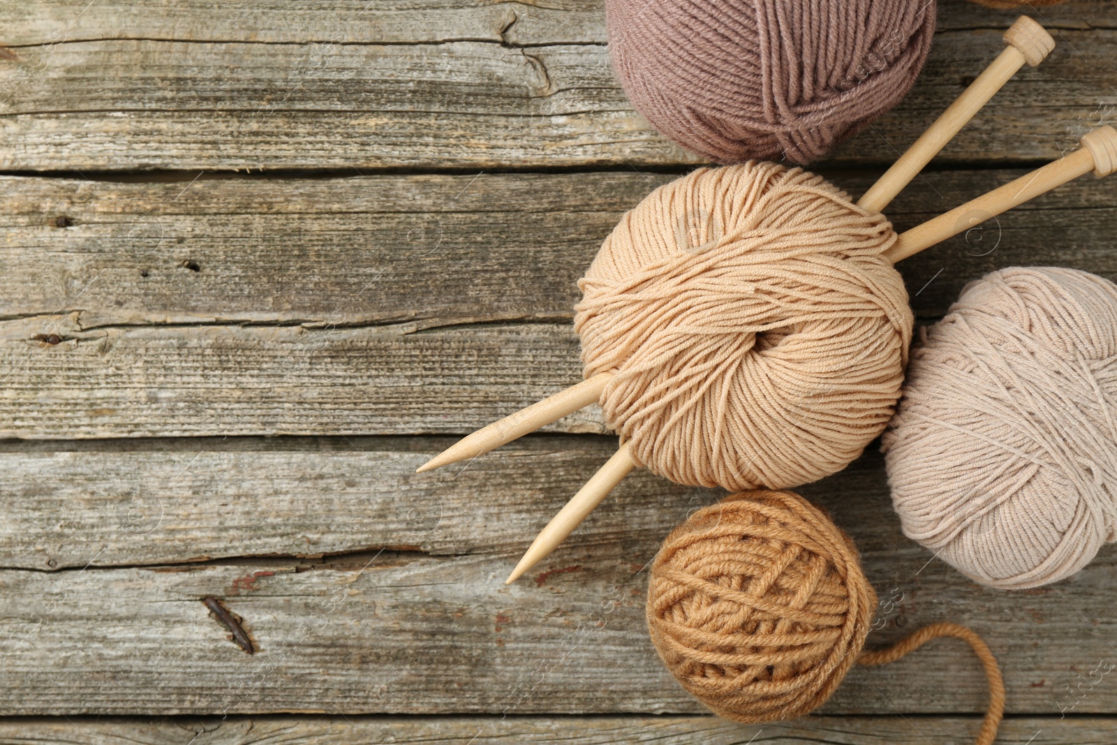 Photo of Skeins of soft yarn and knitting needles on wooden table, top view. Space for text