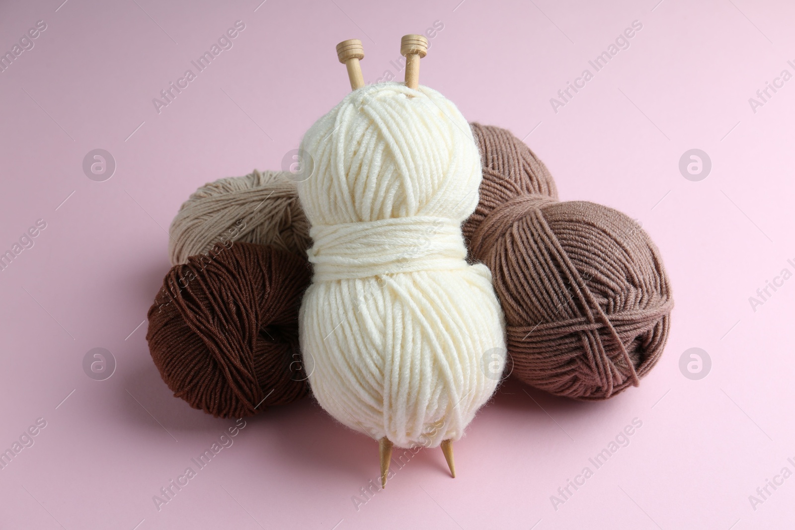 Photo of Skeins of yarn and knitting needles on pink background